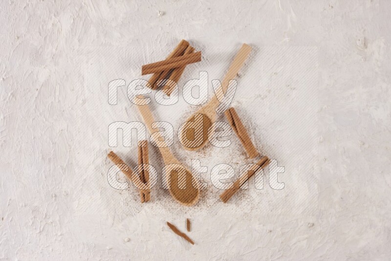 Two wooden spoons full of cinnamon powder with cinnamon sticks on white background