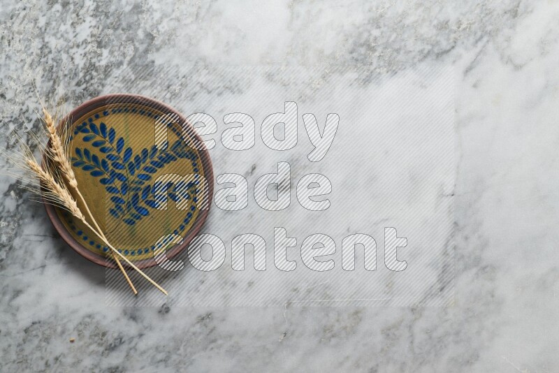 Wheat stalks on decorative pottery plate on grey marble background