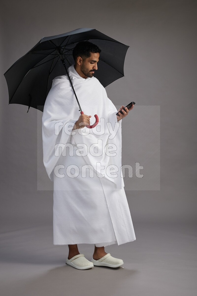 A man wearing Ehram Standing holding umbrella on gray background