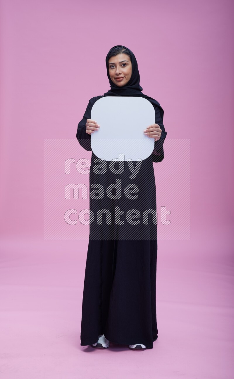 Saudi woman wearing pink ribbon on Abaya standing holding social media signs on pink background
