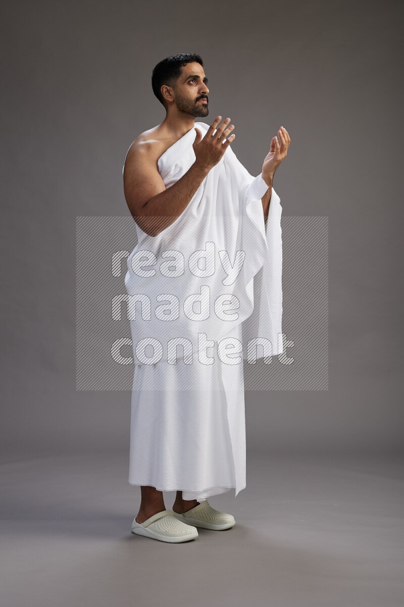 A man wearing Ehram Standing performing dua'a on gray background