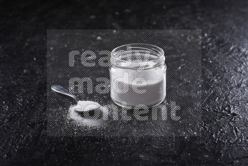 A glass jar full of fine table salt on black background