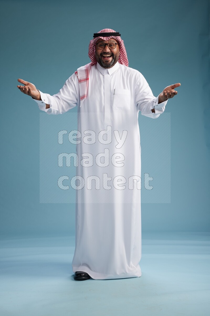 Saudi Man with shimag Standing Interacting with the camera on blue background