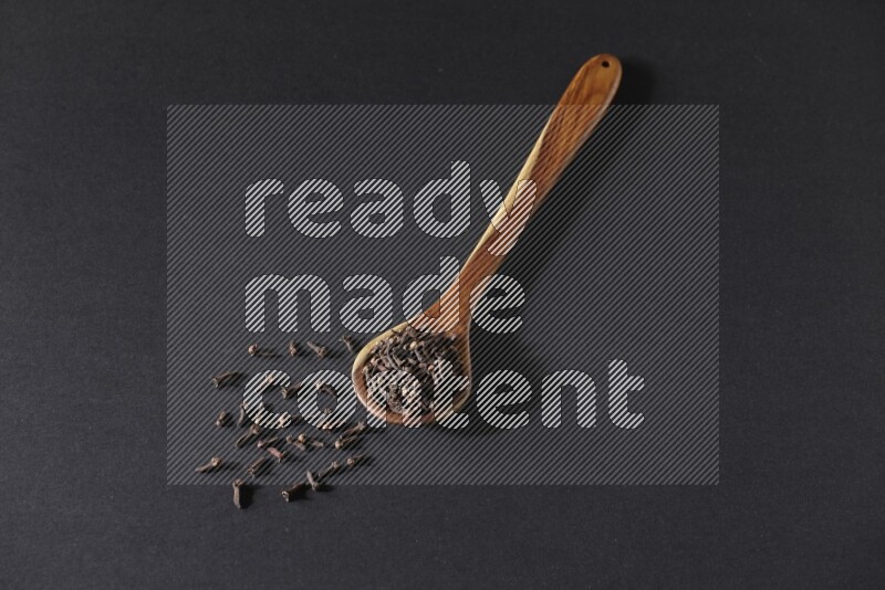 A wooden ladle full of whole cloves on a black flooring