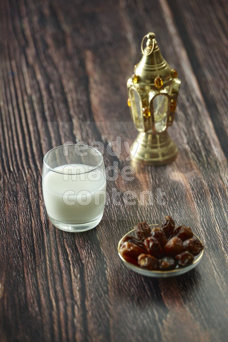 A golden lantern with different drinks, dates, nuts, prayer beads and quran on brown wooden background