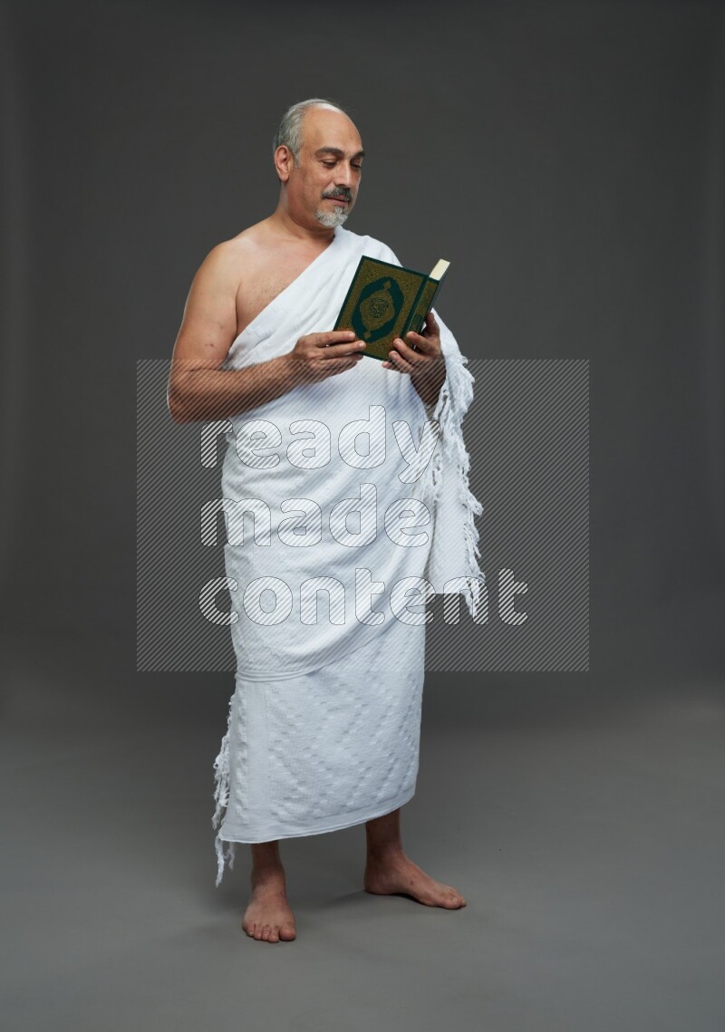 A man wearing Ehram Standing reading quran on gray background