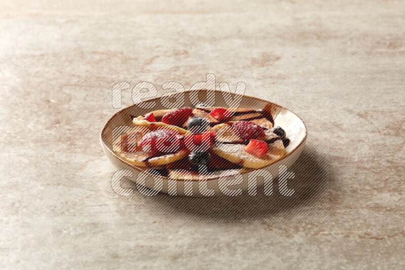 Five stacked mixed berries mini pancakes in an irregular plate on beige background