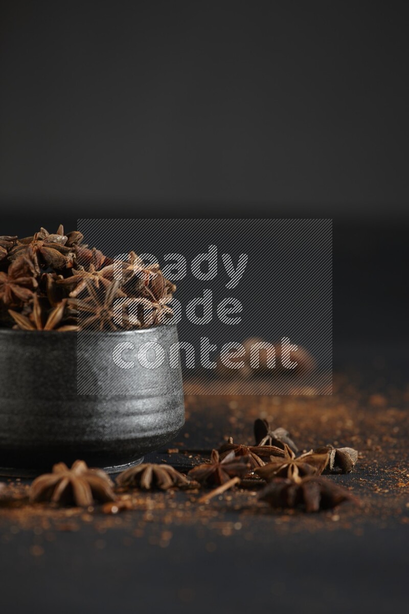 Star Anise in a black bowl with sprinkled anise on black flooring