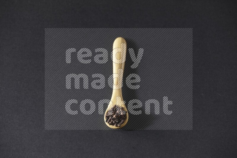 A wooden spoon full of cloves on a black flooring