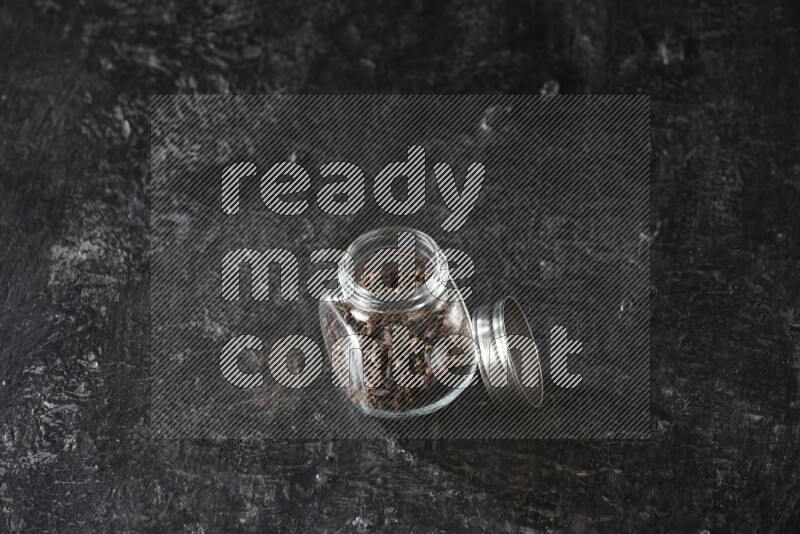 وعاء بهارات زجاجي ممتلئ بحبوب القرنفل على أرضية سوداء