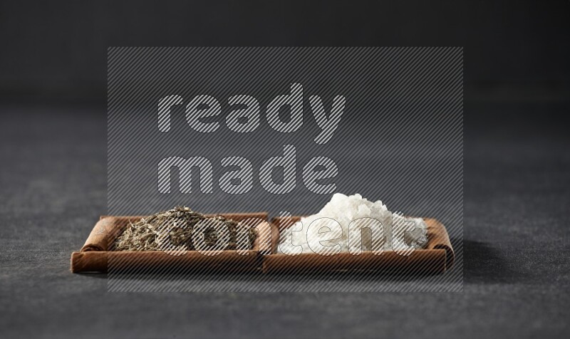 مربعان من أعواد القرفة ممتلئان بالملح الأبيض وحبوب الكمون علي خلفية سوداء