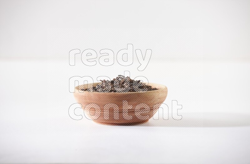 A wooden bowl full of cloves on a white flooring