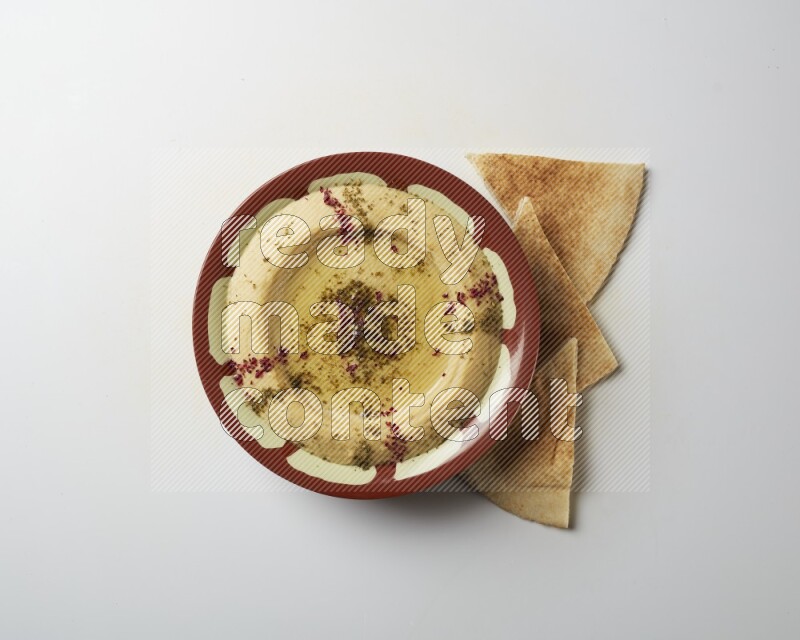 Hummus in a traditional plate garnished with zaatar & sumak on a white background