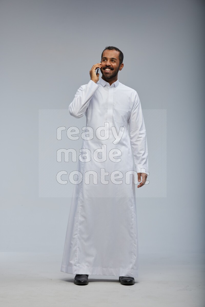 Saudi man wearing Thob standing talking on phone on Gray background