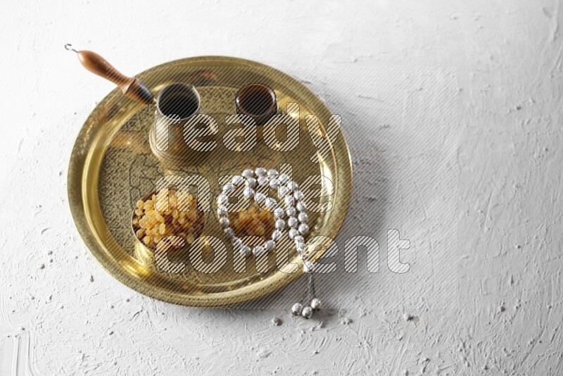 Raisins in a metal bowl with coffee and prayer beads on a tray in a light setup