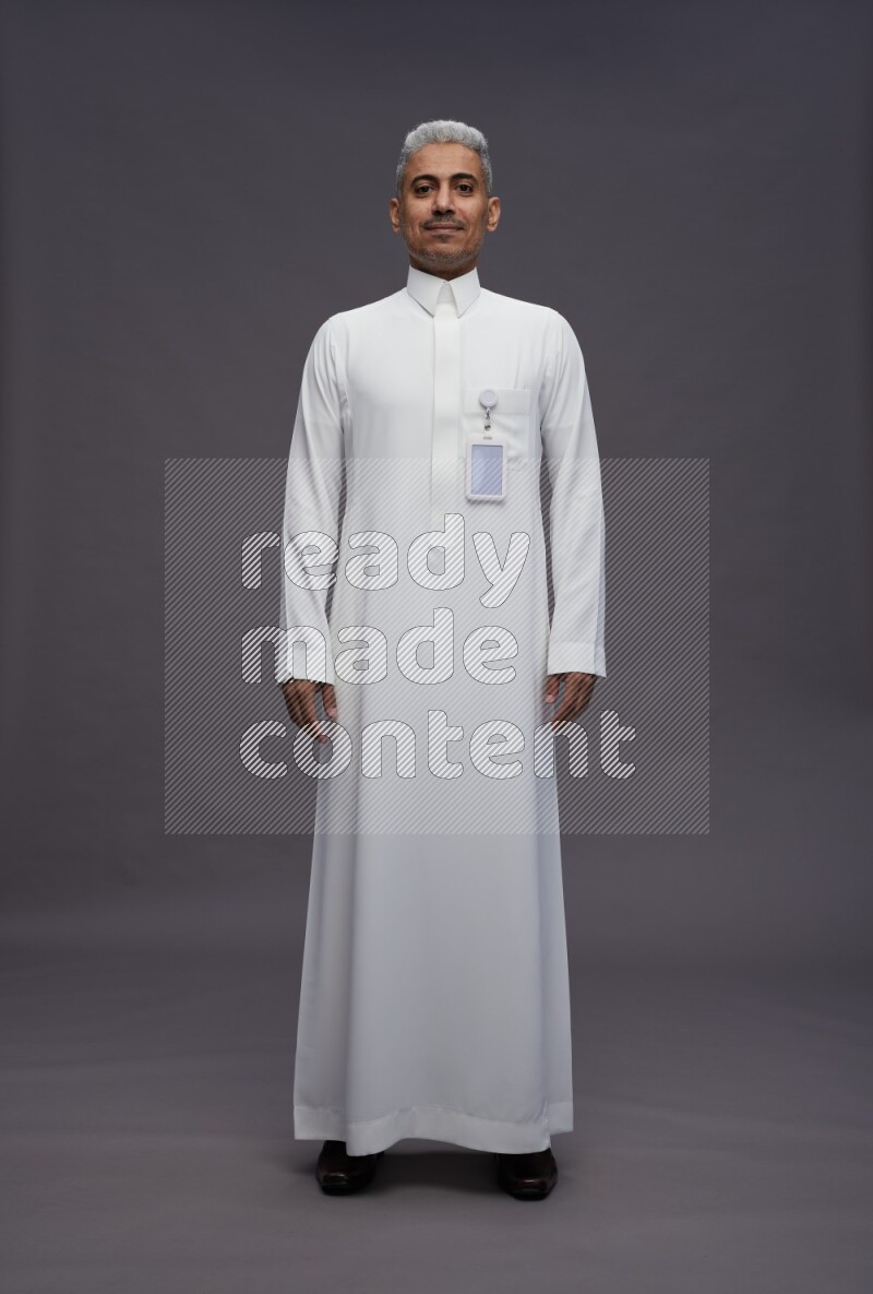 Saudi man wearing thob with pocket employee badge standing interacting with the camera on gray background