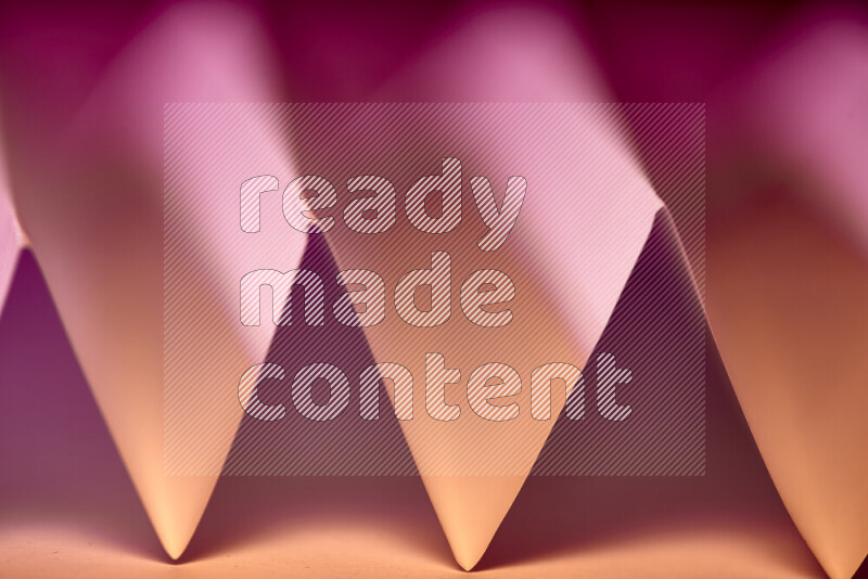 A close-up abstract image showing sharp geometric paper folds in pink gradients and warm tones