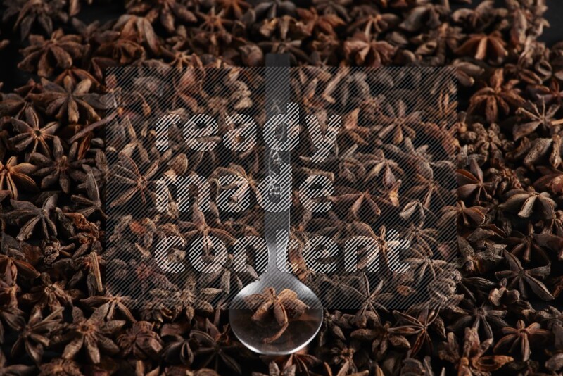 Star Anise in a metal spoon on more stars anise filling the frame on black flooring