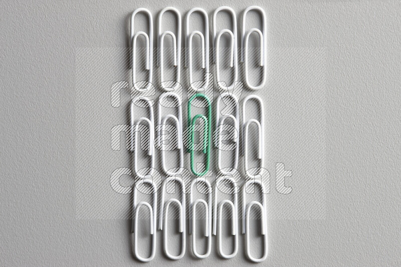 A bunch of white paper clips with a different colored paper clip in the center on grey background