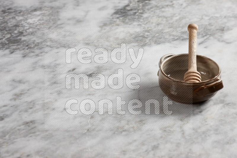 Multicolored pottery bowl with wooden honey dipper in it on grey marble background