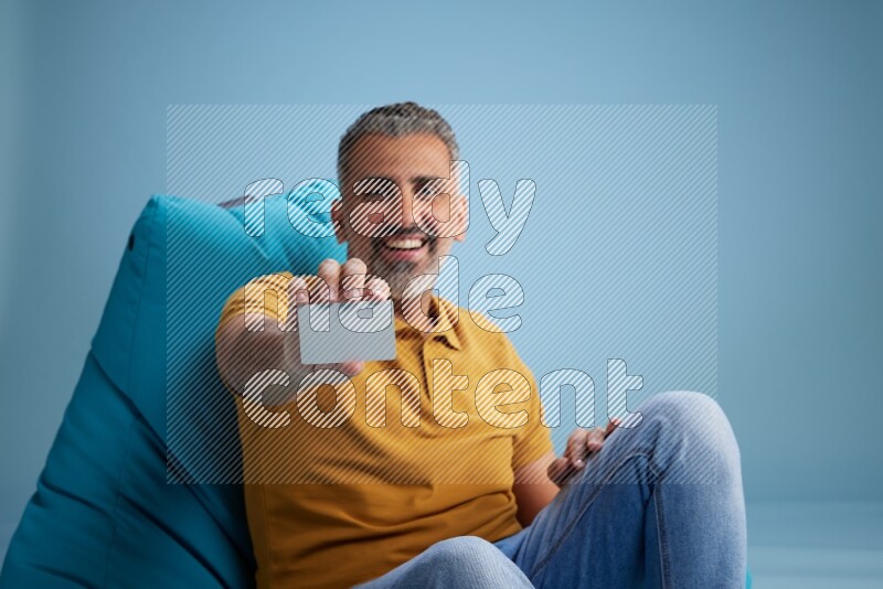 A man sitting on a blue beanbag and holding ATM card