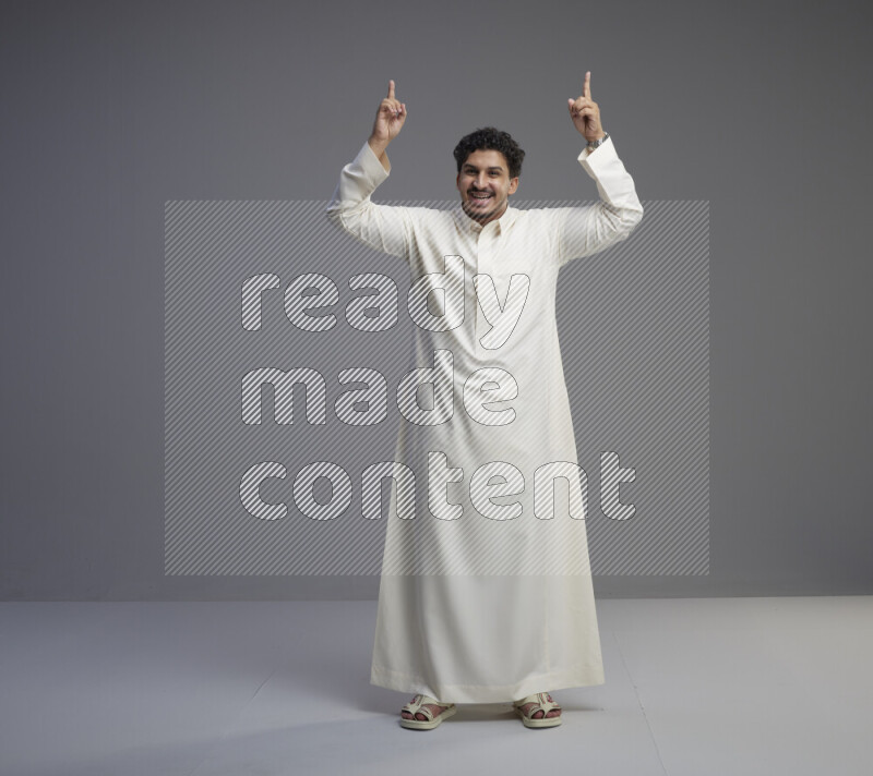 A Saudi man standing wearing thob interacting with the camera on gray background
