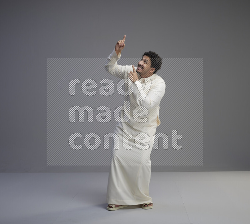 A Saudi man standing wearing thob interacting with the camera on gray background