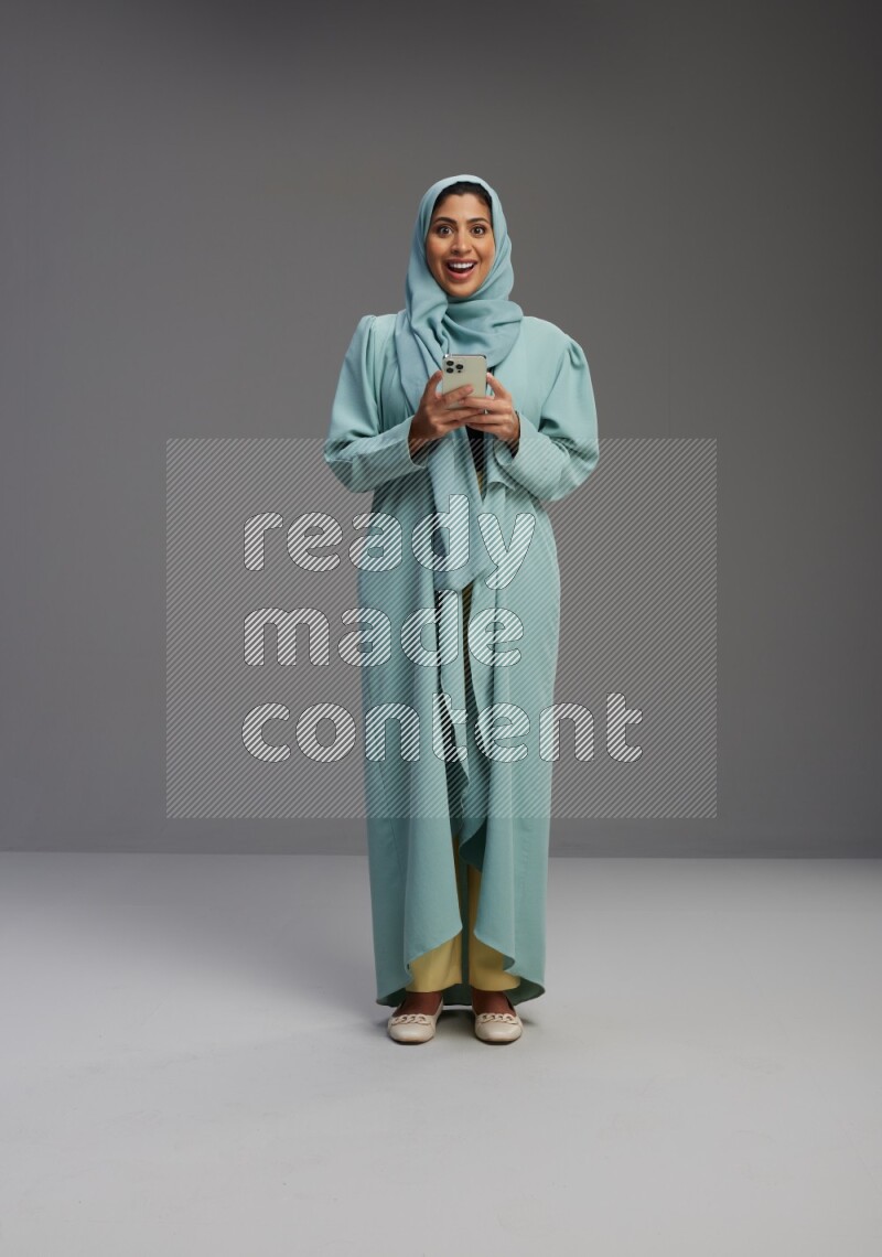 Saudi Woman wearing Abaya standing texting on phone on Gray background