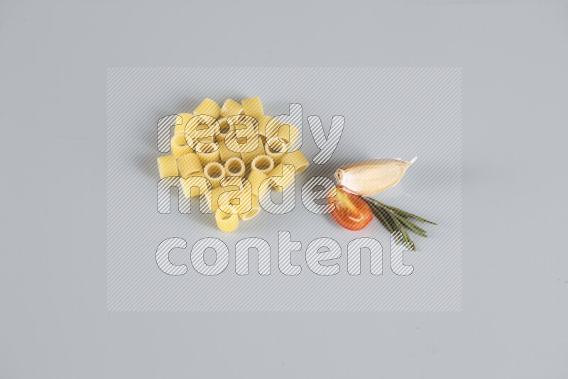 Raw pasta with different ingredients such as cherry tomatoes, garlic, onions, red chilis, black pepper, white pepper, bay laurel leaves, rosemary, cardamom and mushrooms on light blue background