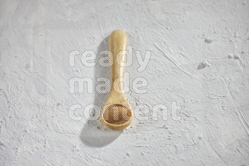 Cinnamon powder in a wooden spoon on a white background