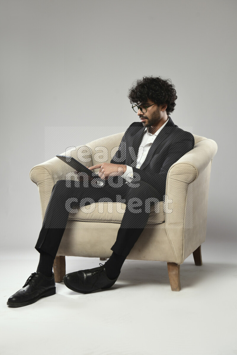 A man wearing formal sitting on a chair browsing on a tablet on white background