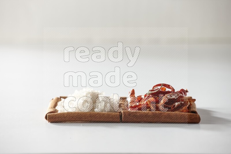 2 squares of cinnamon sticks full of dried red chilis and white salt on white flooring