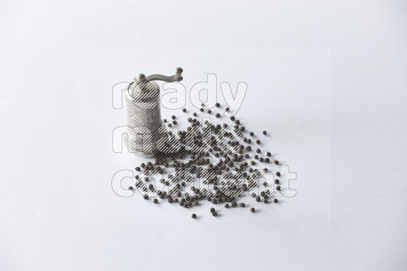 A turkish metal pepper grinder and spreaded black pepper beads on a white flooring