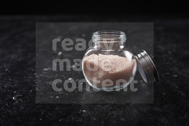 A glass jar full of fine himalayan salt on black background