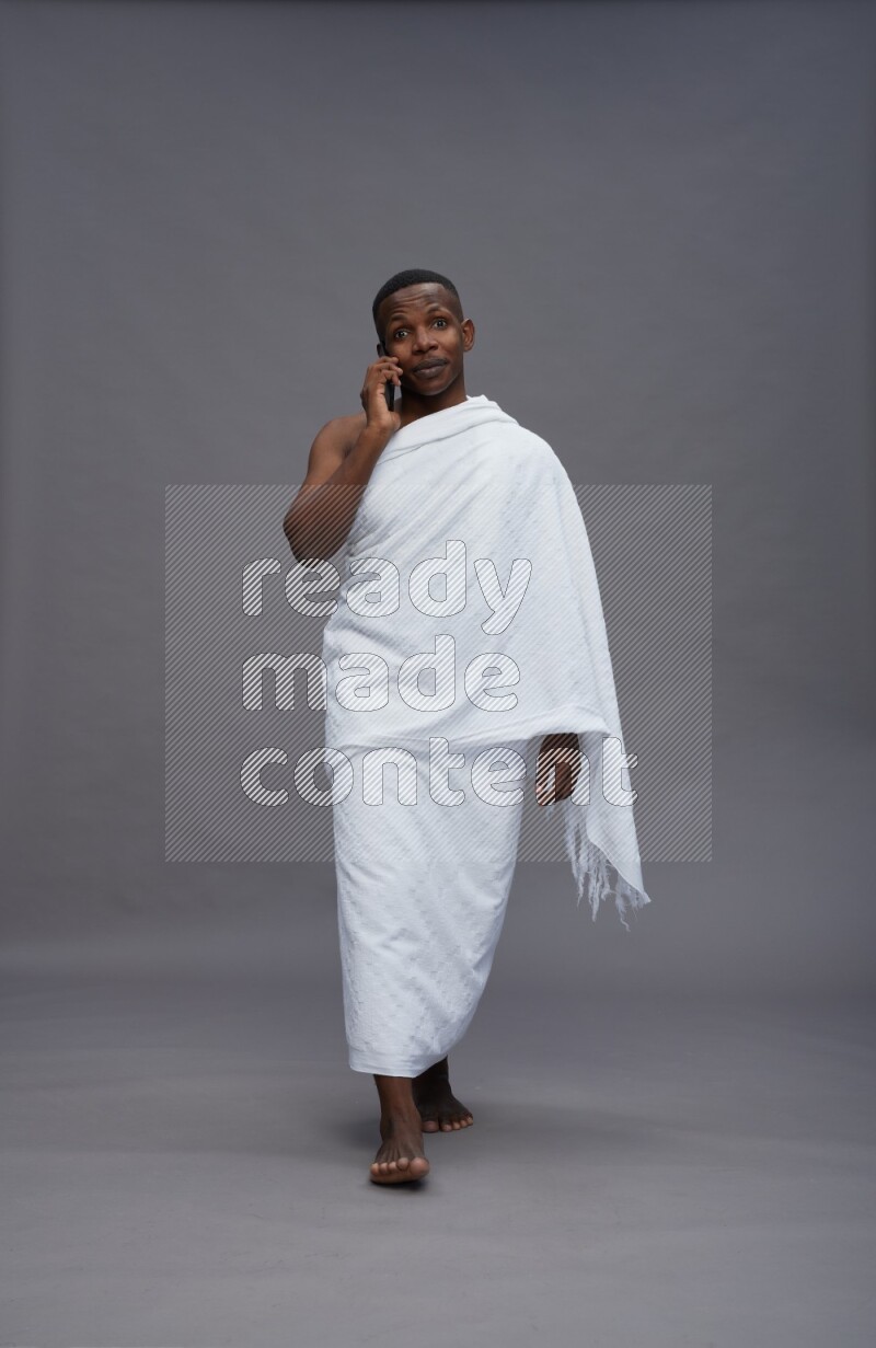 A man wearing Ehram Standing talking on phone on gray background