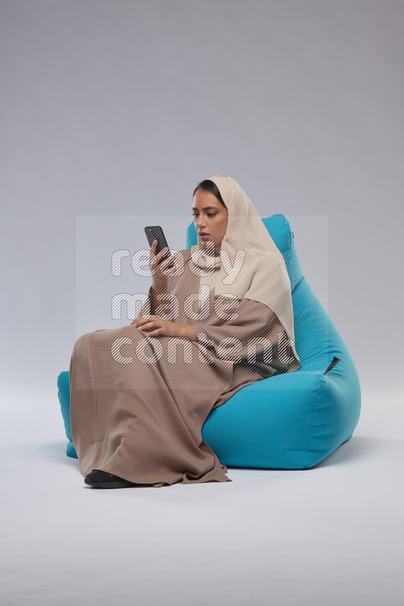 A Saudi woman sitting on a blue beanbag and texting on phone