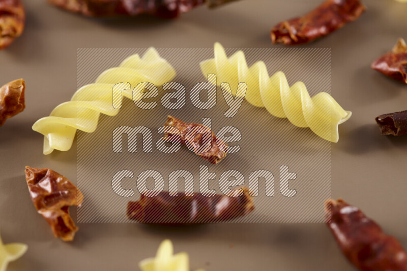 Raw pasta with different ingredients such as cherry tomatoes, garlic, onions, red chilis, black pepper, white pepper, bay laurel leaves, rosemary and cardamom on beige background