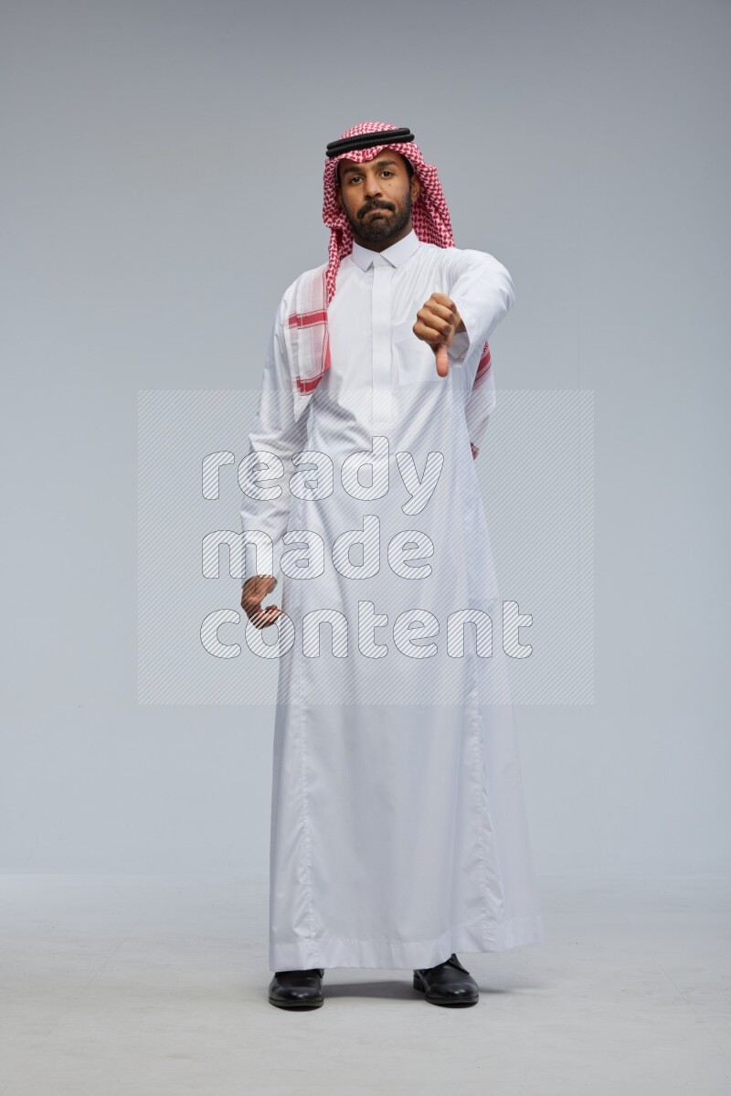 Saudi man Wearing Thob and shomag standing interacting with the camera on Gray background