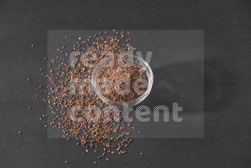 وعاء زجاجي ممتلئ بحبوب بذر الكتان محاط بالبذور على أرضية سوداء