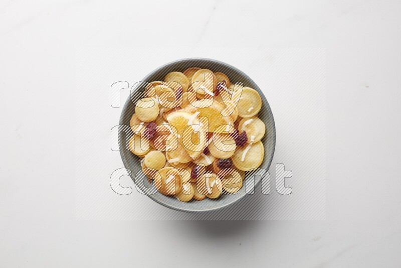 Top-view shot of orange candy cereal pancakes in a round bowl on white background
