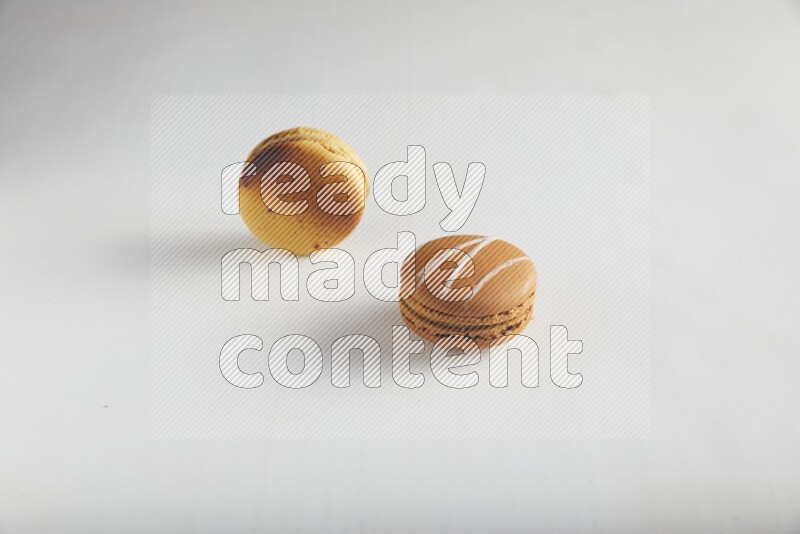 45º Shot of of two assorted Brown Irish Cream, and Yellow Crème Brulée macarons on white background
