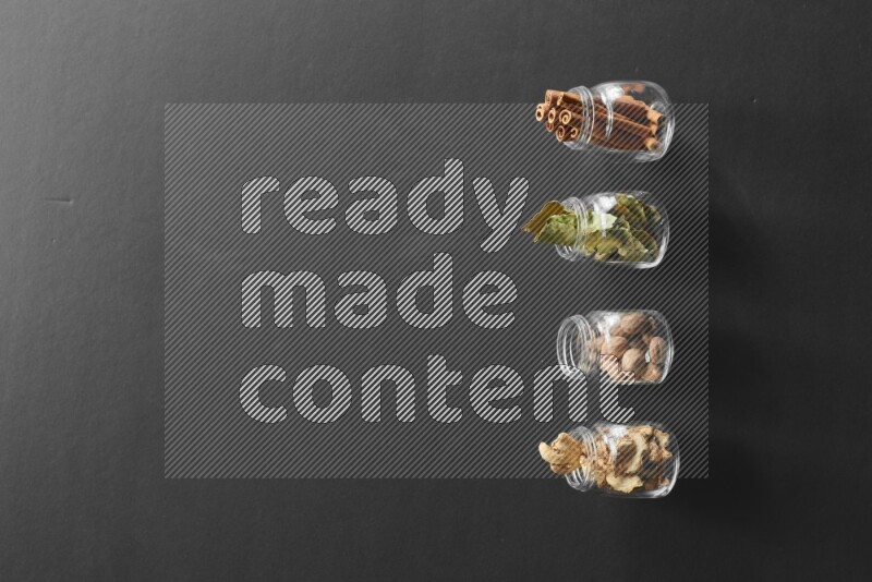 أوراق الغار وزنجبيل مجفف وقرفة وجوزة الطيب في أوعية زجاجية علي خلفية سوداء