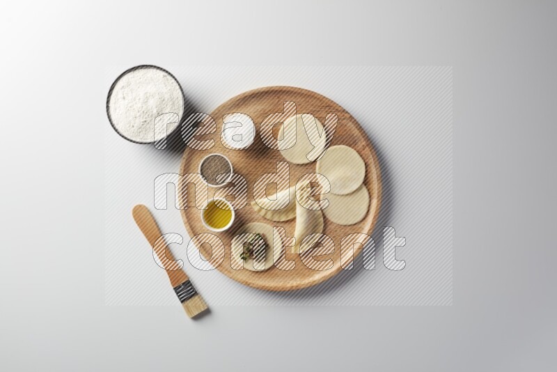 two closed sambosas and one open sambosa filled with meat while flour, salt, black pepper and oil with oil brush aside in a wooden dish on a white background