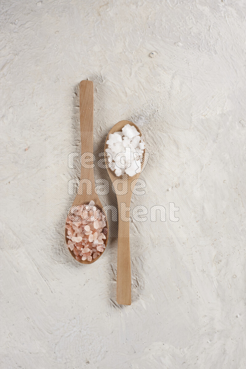2 wooden spoons filled with fine and coarse salt on white background