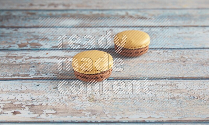 45º Shot of two Yellow and Brown Chai Latte macarons on light blue wooden background