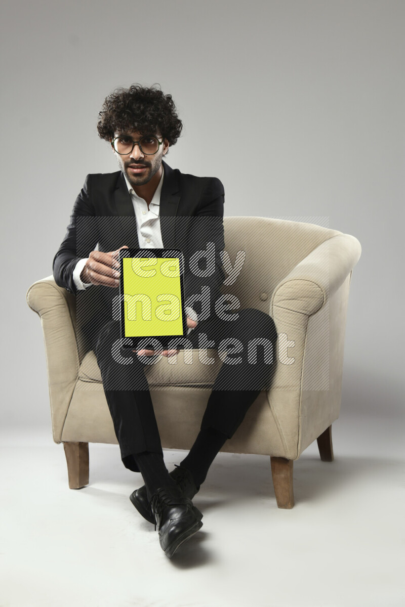 A man wearing formal sitting on a chair showing a tablet screen on white background