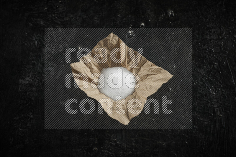 A crumpled piece of paper full of white salt on black background