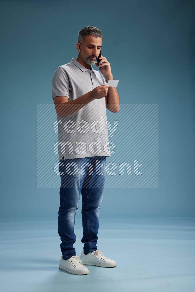 Man Standing holding ATM while talking on phone on blue background