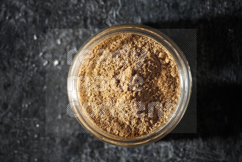 A glass jar full of allspice powder on a textured black flooring