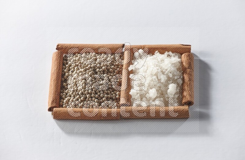 2 squares of cinnamon sticks full of white pepper and white salt on white flooring